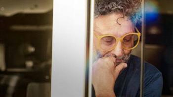 Fito Páez in yellow glasses thinking, seen through reflective glass.