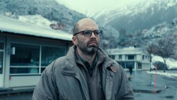 Fjord: A bald White man with glasses looks concerned, standing in front of a building with snowy mountains in the background