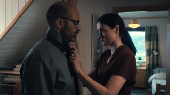 Fjord: A woman adjusts her husband's tie as they both look serious standing in the hallway of their home
