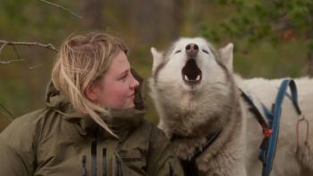 Folktales Movie: Woman in a coat sits beside a howling husky in an outdoor setting.