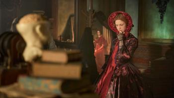 Frankenstein Movie: Elizabeth (Mia Goth), in a red dress, explores a study cluttered with books and a model of a human head
