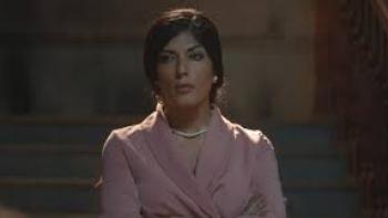 From the Ashes Movie: Woman in pink suit and pearls looks serious