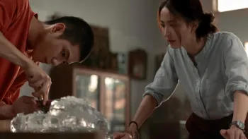 Frozen Hot Boys movie: Thai older teen boy in red t-shirt left picks at a mound of ice while Thai woman in light blue shirt right looks on