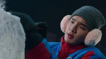 Frozen Hot Boys movie: Thai older teen in red and blue coat, hat, and pink earmuffs, right, works on ice sculpture outside at night 