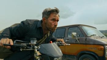 Get Fast movie: White man in black jacket rides motorcycle center next to brown and yellow van right