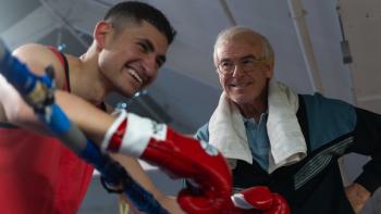 Giant: Young boxer smiling with a coach, leaning on boxing ring ropes