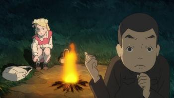 Giovannis Island movie: Junpei and Tanya are around a campfire at night, Tanya is sitting reaching for her book bag, while Junpei is standing looking nervous and grasping his chin.
