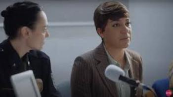 Girl in the Video movie: Two people seated at a table with microphones, one in a suit, the other in a uniform.