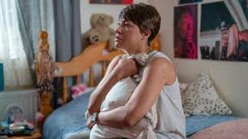 Girl in the Video movie: Black Woman sitting on a bed, hugging a pillow, looking contemplative.