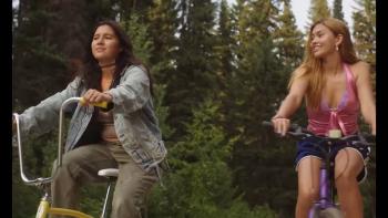 Girls Like Girls movie photo: Two young women riding bikes in a rural setting, smiling