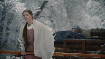 Go West Movie: White woman in prairie garb walks through a snowy trail carrying a handcart with another woman lying in it