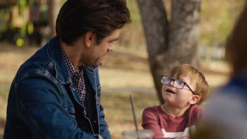 God's Country Song: A man looks at a younger boy who is looking back at him mid conversation in a scene from God's Country Song