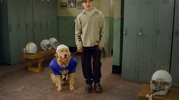Air Bud: Golden Receiver Movie: A golden retriever wearing a soccer jersey and helmet stands next to a White boy in a sweatshirt inside a locker room