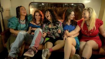 Greatest Days: Five teenage girls sit on the back seat of a bus, smiling and laughing