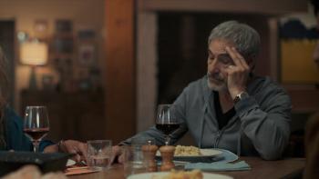 GTMax movie: White French man right sits at dinner table with hand on his forehead, wine and food before him
