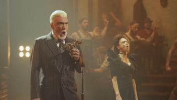 Hadestown the Musical: A man (Patrick Page) sings into an old-timey mic near his wife, Persephone (Amber Gray)