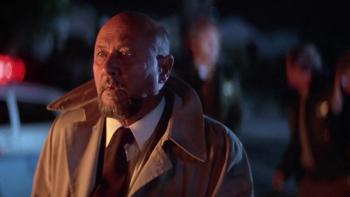 Halloween II: Donald Pleasance looks serious as he stands in a street with policemen and police cars in the background