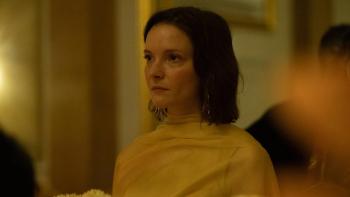 Hamlet: Morfydd Clark looks serious as she stands in a room with other people blurred on the edges of the shot