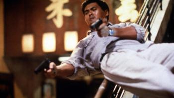 Hard Boiled: Chow Yun-Fat slides down a banister on his back, firing two pistols
