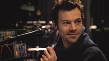 Harry Styles — One Night in Manchester: Harry Styles stands behind a tech desk with a microphone pointed toward him