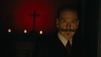 A Haunting in Venice Movie: Detective Hercule Poirot looking pensive, stands in front of a wall with the shadow of a cross