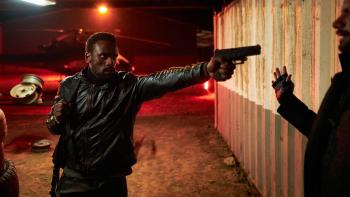 Heart of the Hunter movie: South African Black man left points gun at man on right next to shipping container