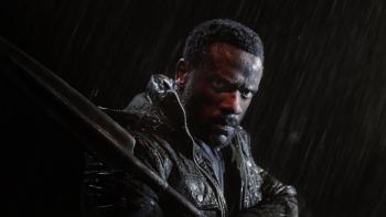 Heart of the Hunter movie: South African Black man in black jacket and spear center stands in the rain