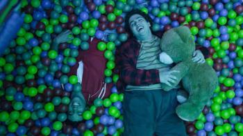 Here the Whole Time: Two people laughing in a ball pit, one holding a teddy bear.