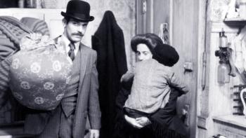 Hester Street: Steven Keats holds a large bag as he stands inside the door of an apartment, Carol Kane standing behind him holding their young son