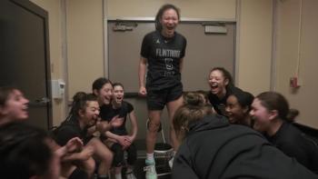Home Court movie: A team is seated in a circle while Ashley Chea stands seeming to lead the team in a yell