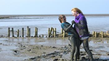 Of Girls and Horses Movie: Two people joyfully playing in a muddy beach setting.