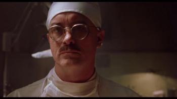 House on Haunted Hill: Dr. Vannacutt in old-fashioned surgical scrubs in a dark room looking serious