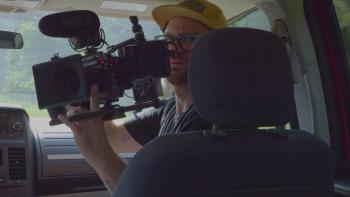 House on Eden Movie: In the passenger seat of the van, Jay poses while holding an elaborate video camera