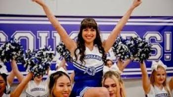 Identity Theft of a Cheerleader: Cheerleader lifted by teammates, smiling with arms raised, in front of "Cougars" banner.