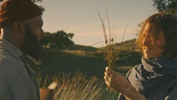 Harvest: A White man shows a plant to a Black man wearing a hat