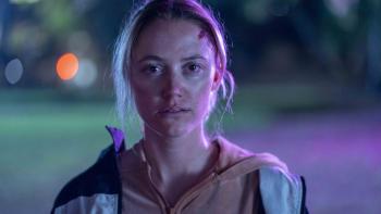 In Cold Light movie: Ava (Maika Monroe), looks at the camera, bloody cuts on her face and wearing two zip up hoodies