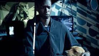 In His Shadow: Black blind man sits at desk with cane and dog by his side