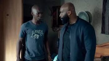 In His Shadow: Standing Black man on left faces standing Black man on right