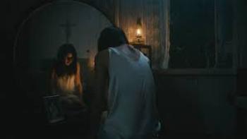 In My Mother's Skin movie: Filipino woman center in white negligee hunches in front of mirror in dark bedroom with reflection showing a cross above her head