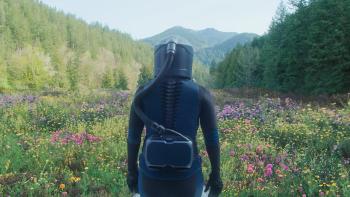 In the Blink of an Eye movie: Kate McKinnon in a head to toe space suit walks into a green mountainous landscape