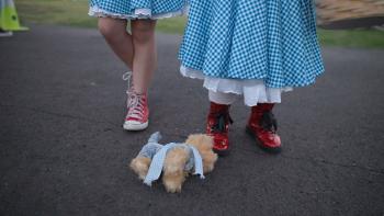 It’s Dorothy! movie: two sets of children’s legs, both wearing blue gingham dresses and red shoes, plush dog toy on ground
