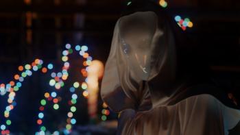 It's a Wonderful Knife Movie: The killer, wearing a white mask hooded cloak, pauses in front of colored Christmas lights