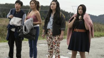 Joy Ride: Four Asian women stand with their arms full of belongings against an empty rural landscape. They all look distressed; one in particular has a downturned mouth and slumped shoulders. 
