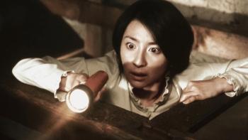 Ju-On—The Grudge: Woman looking surprised while holding a flashlight in a dimly-lit space