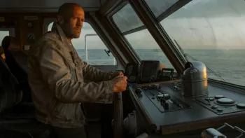 Mutiny: Shaved-headed man in denim jacket steering a boat at sunset through large windows
