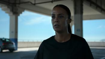K.O. movie: Algerian French woman in black shirt stands alone in an almost empty parking ramp structure