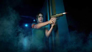 K.O. movie: Algerian French woman with police arm band holds gun with two hands while firing in a dark hallway