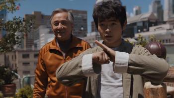 Karate Kid: Legends movie: Shifu Han (Jackie Chan) stands smiling behind Li Fong (Ben Wang), who looks ready for action