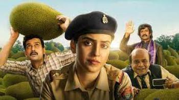 Kathal - A Jackfruit Mystery: a female soldier looks at camera with men in background, including one with a jackfruit