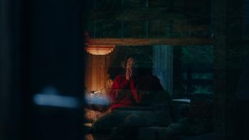Keeper Movie: Seen through a window, Liz (Tatiana Maslany) sits on a couch holding her hands to her face as if terrified